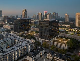 Cityscape with high-rise buildings during dusk, featuring modern architecture, illuminated windows, and a visible highway.