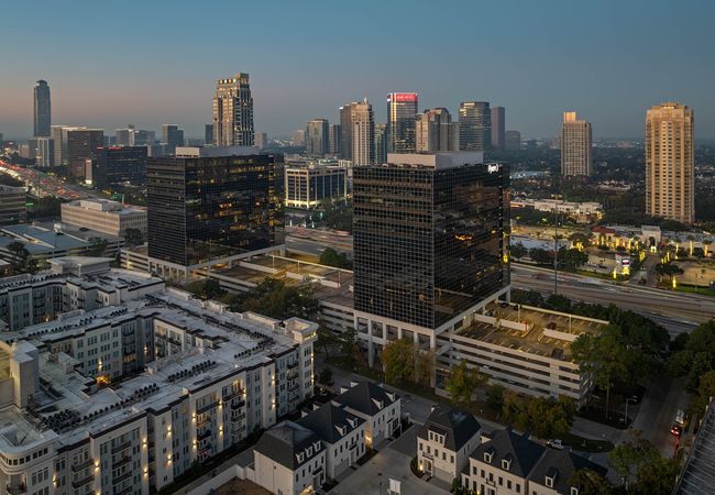 Cityscape with high-rise buildings during dusk, featuring modern architecture, illuminated windows, and a visible highway.