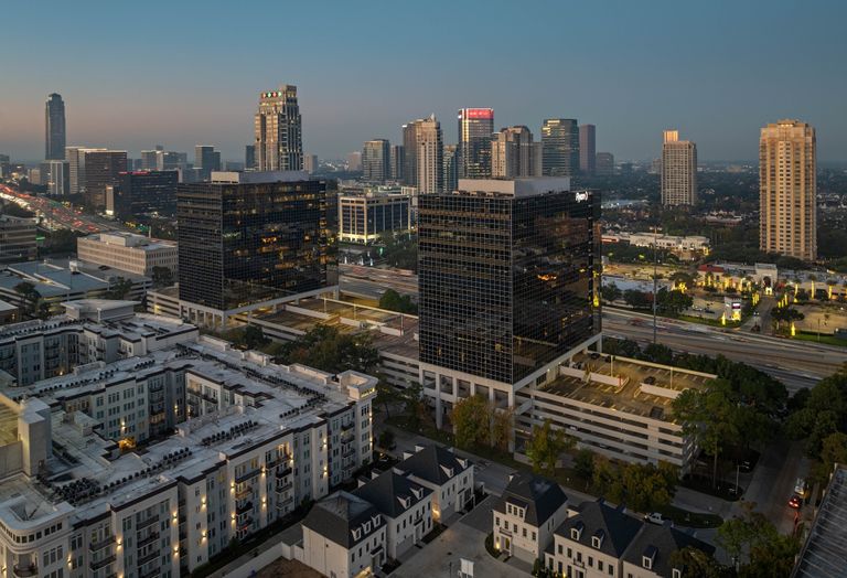 Cityscape with high-rise buildings during dusk, featuring modern architecture, illuminated windows, and a visible highway.