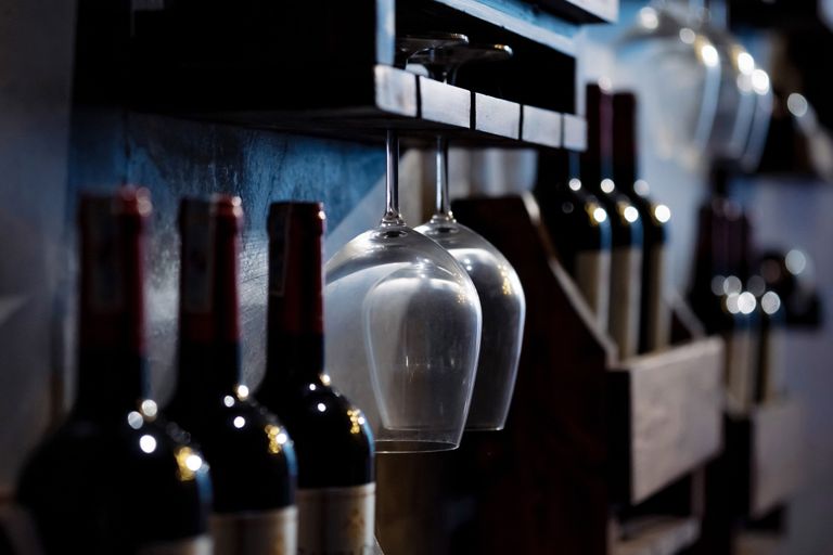 Wine bottles and inverted wine glasses stored on wooden shelves in a dimly lit cellar.