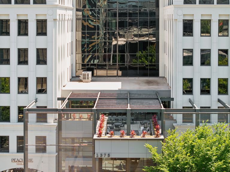 Exterior of a modern office building with reflective glass windows, white facade, and a rooftop terrace adorned with planters and seating.