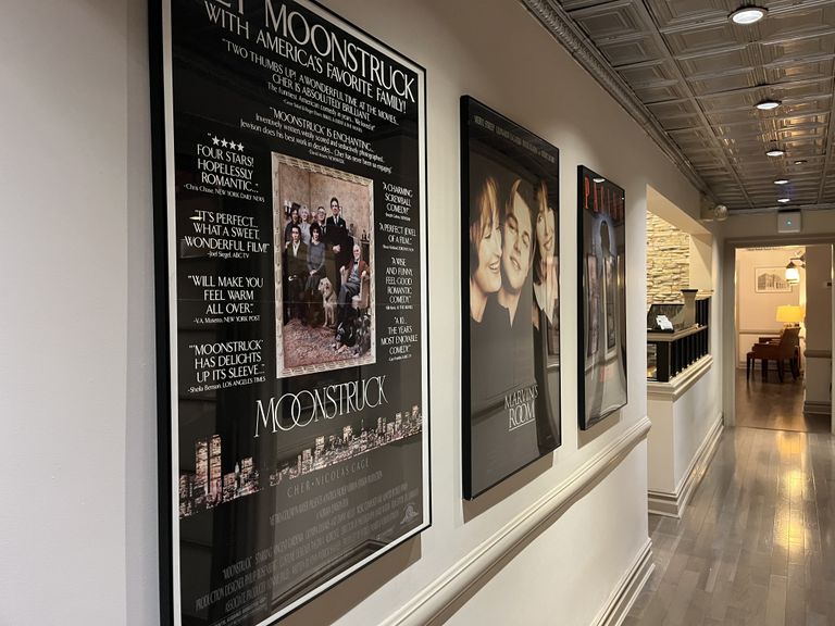 A hallway with framed movie posters including "Moonstruck" and "Marvin's Room" on the wall, with warm lighting and wooden flooring.