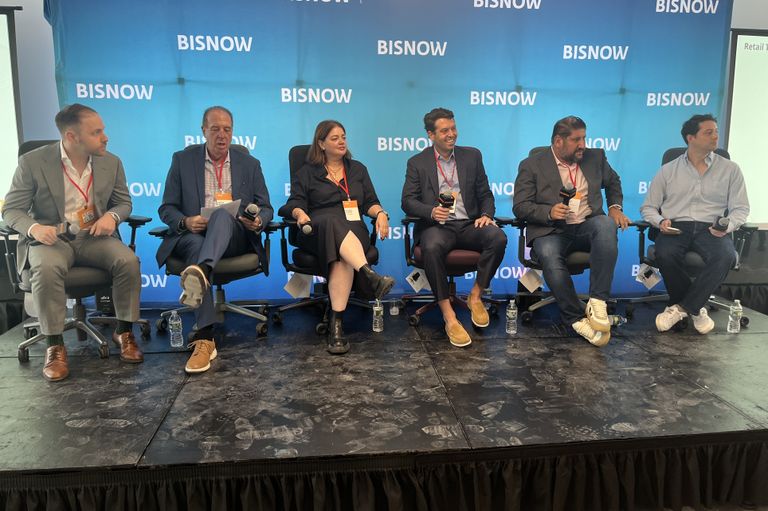 Six people with microphones sit on a panel stage with a Bisnow backdrop, participating in a conference or discussion.