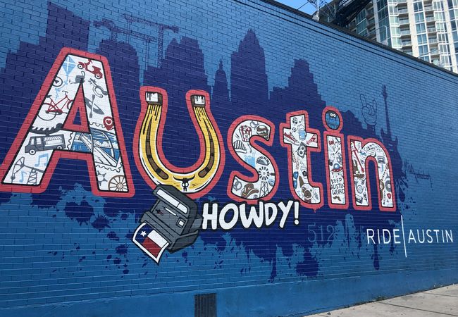 Colorful mural on a blue brick wall with the word "Austin," featuring Texas-themed icons and the phrase "Howdy!".