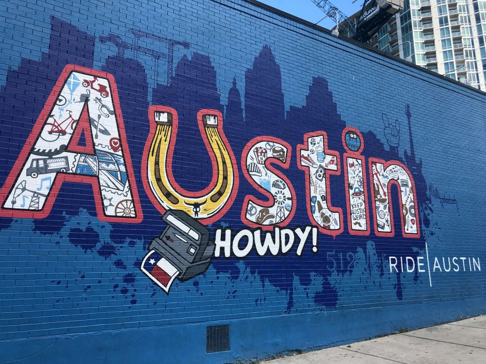 Colorful mural on a blue brick wall with the word "Austin," featuring Texas-themed icons and the phrase "Howdy!".
