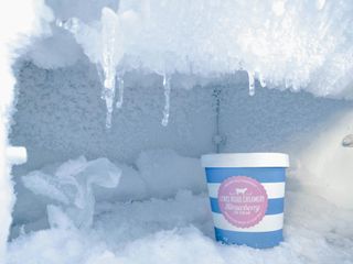 A container of strawberry ice cream in a frost-covered freezer with icicles hanging from the top.