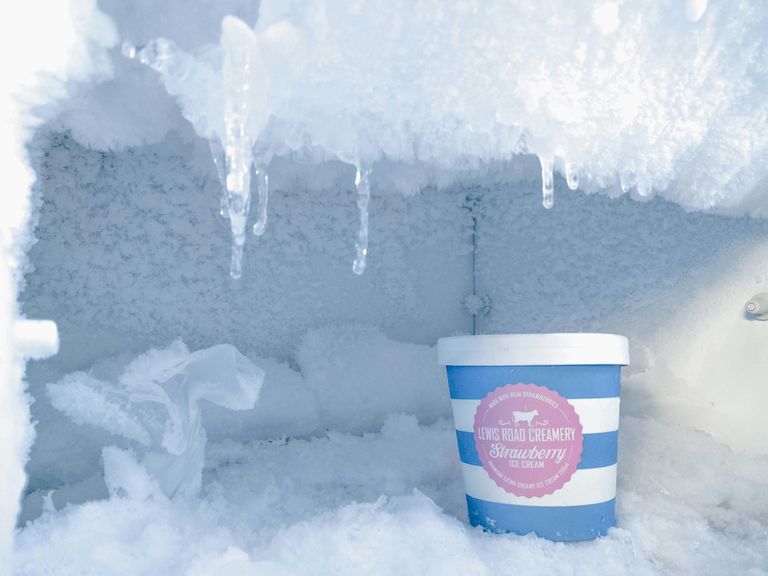 A container of strawberry ice cream in a frost-covered freezer with icicles hanging from the top.