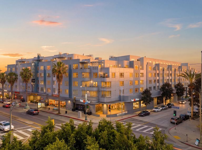 Urban building at sunset, featuring FedEx Office and Chipotle on the ground floor, with palm trees and cars on the street.