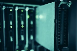 Close-up of a row of server racks in a data center, with one rack pulled out slightly, illuminated by soft green lighting.