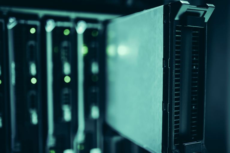 Close-up of a row of server racks in a data center, with one rack pulled out slightly, illuminated by soft green lighting.