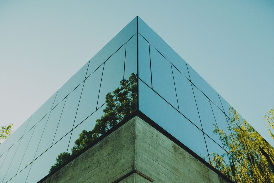 An office building reflecting green trees in the glass