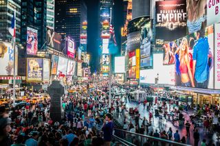 A bustling Times Square at night with bright billboards, neon lights, and a large crowd of people and cars on the busy streets.