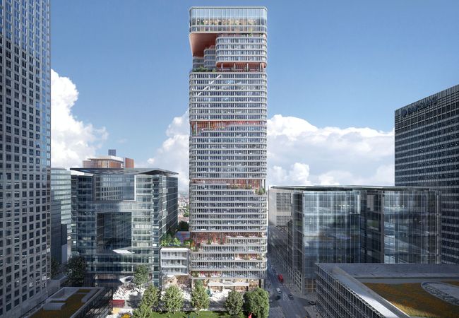 A modern cityscape with a tall, sleek skyscraper featuring curved balconies and adjacent contemporary glass buildings under a clear blue sky.