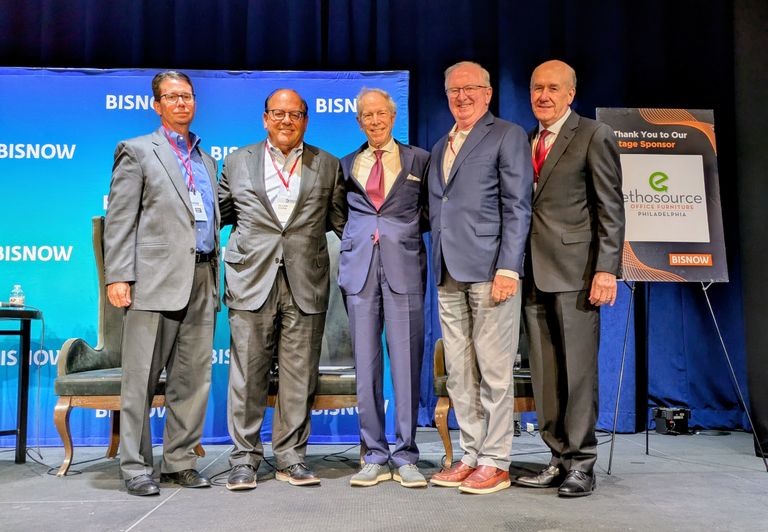 Five men in business suits stand together on a stage with the "BISNOW" backdrop and a sponsor sign.
