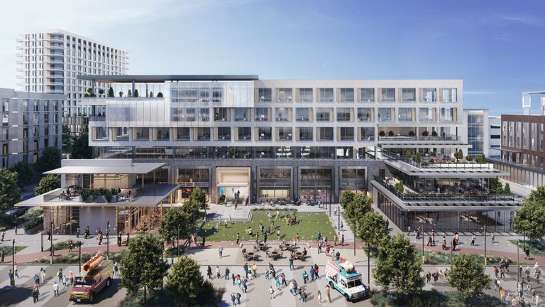 Modern multi-story building with glass facades, surrounded by people, trees, and food trucks on a sunny day.