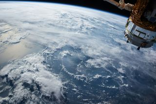 View of Earth from space, showing a large expanse of clouds over the ocean and part of a satellite.