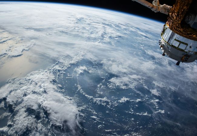 View of Earth from space, showing a large expanse of clouds over the ocean and part of a satellite.