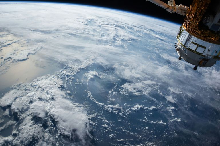 View of Earth from space, showing a large expanse of clouds over the ocean and part of a satellite.