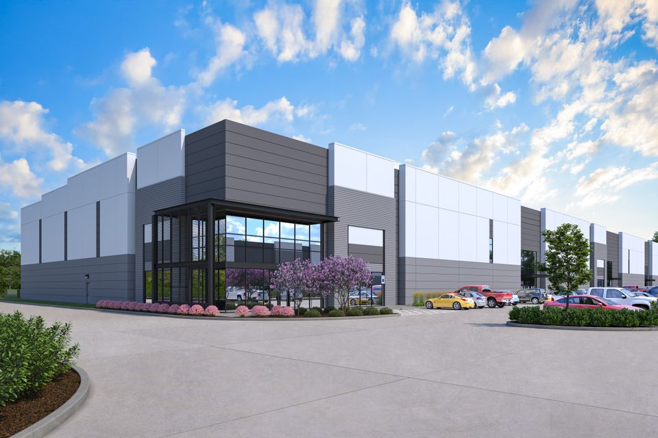 Modern industrial building with a parking lot, purple flowering shrubs, and a clear blue sky.