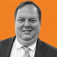 A man in a suit and tie smiling against an orange background with subtle, wavy lines.