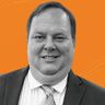 A man in a suit and tie smiling against an orange background with subtle, wavy lines.