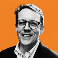 Man wearing glasses and a suit, smiling against an orange background with subtle wave patterns.
