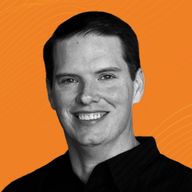 Smiling man with short dark hair wearing a black shirt against an orange background.