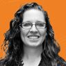 A woman with curly hair and glasses smiles against an orange background with subtle wave patterns.