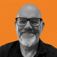 A smiling man with glasses and a beard against an orange background.
