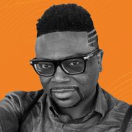 Man with styled hair, geometric designs on the side, wearing black-rimmed glasses and a button-up shirt, set against an orange background.