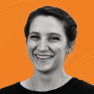 Smiling woman with hoop earrings and a black top against a bright orange background.