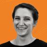 Smiling woman with hoop earrings and a black top against a bright orange background.