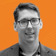 A man wearing glasses and a blazer smiles against an orange background with subtle wave patterns.