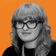 A woman with glasses and curly hair poses against an orange background with subtle wave patterns.