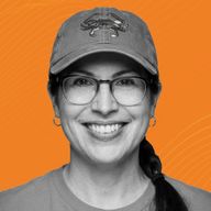Smiling woman wearing glasses and a hat with a crab design, against an orange background.