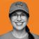 Smiling woman wearing glasses and a hat with a crab design, against an orange background.