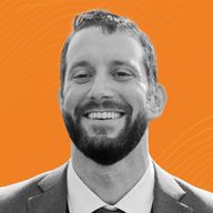 Smiling man with a beard in a suit against an orange background.