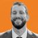 Smiling man with a beard in a suit against an orange background.