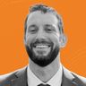 Smiling man with a beard in a suit against an orange background.