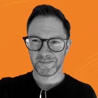 A person with glasses and short hair, wearing a dark shirt, stands against an orange background with subtle wave patterns.