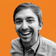Smiling man with short hair and a checkered shirt, set against an orange background.