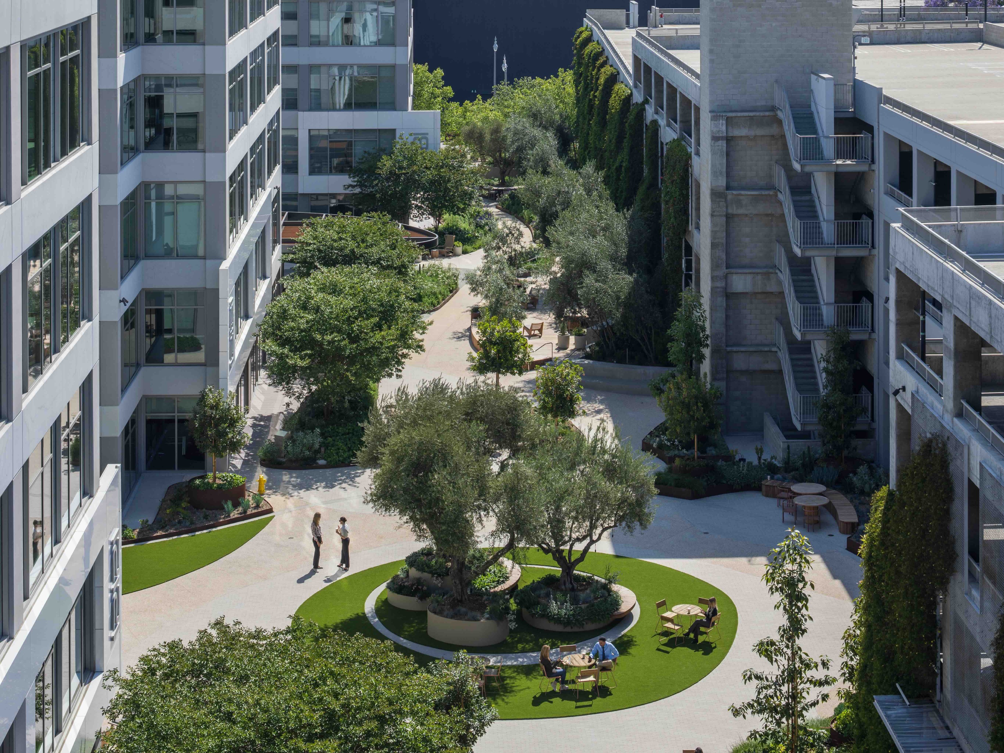 The Bluffs office building, a repositioned office property with a courtyard with trees, seating, and pathways, surrounded by office buildings. Employees are seen walking and sitting on benches.