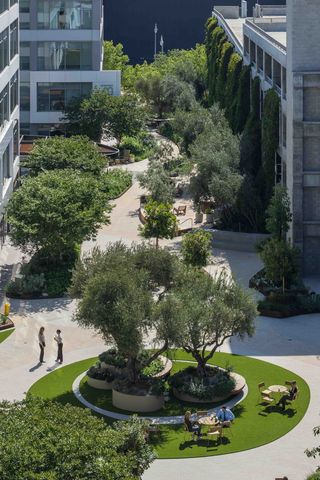 The Bluffs office building, a repositioned office property with a courtyard with trees, seating, and pathways, surrounded by office buildings. Employees are seen walking and sitting on benches.