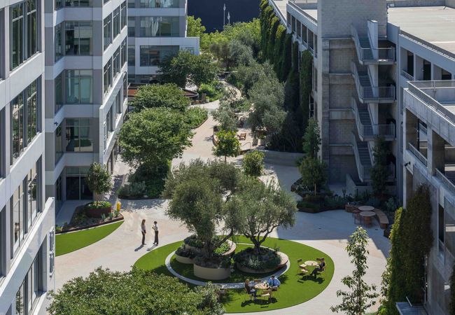 The Bluffs office building, a repositioned office property with a courtyard with trees, seating, and pathways, surrounded by office buildings. Employees are seen walking and sitting on benches.