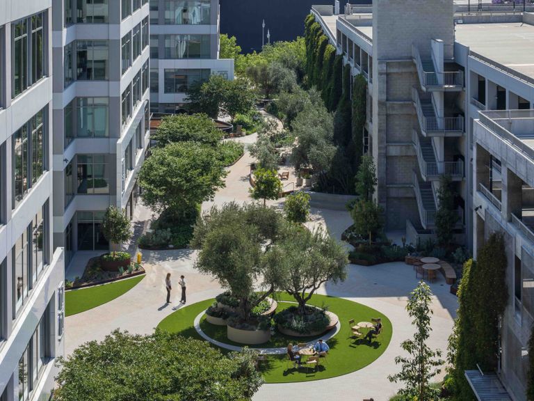 The Bluffs office building, a repositioned office property with a courtyard with trees, seating, and pathways, surrounded by office buildings. Employees are seen walking and sitting on benches.