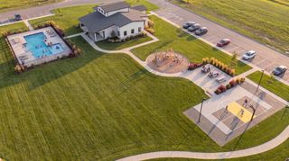Aerial view of a community park with a swimming pool, playground, basketball court, and picnic area surrounded by green lawns and parking spaces.