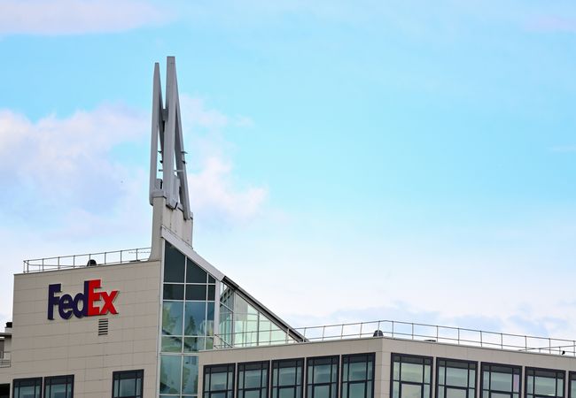 Modern office building with FedEx logo, featuring large windows and distinctive rooftop structures against a blue sky.