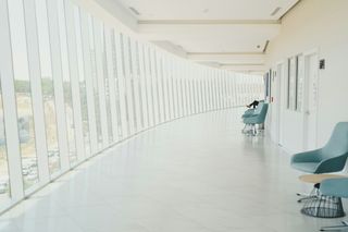 Bright corridor with large windows, light blue chairs, and tables along the right side, creating a calm, open space.