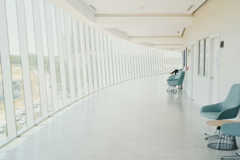 Bright corridor with large windows, light blue chairs, and tables along the right side, creating a calm, open space.