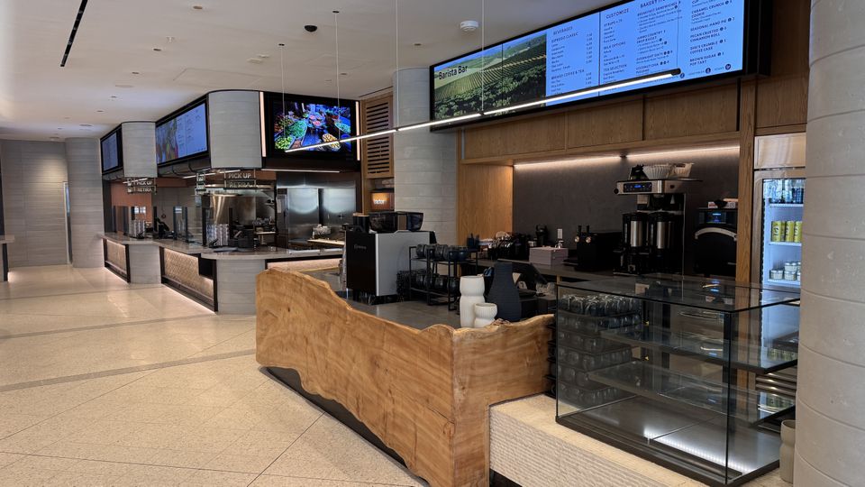 Explorers Eatery with wooden counter, digital menu screens, coffee machines, and a glass display case, reflecting a sleek design.